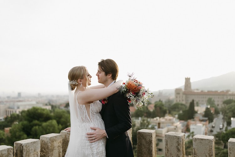 A couple embracing on the stone-crenellated terrace of Bellesguard Tower in Barcelona, with the city and hills behind
