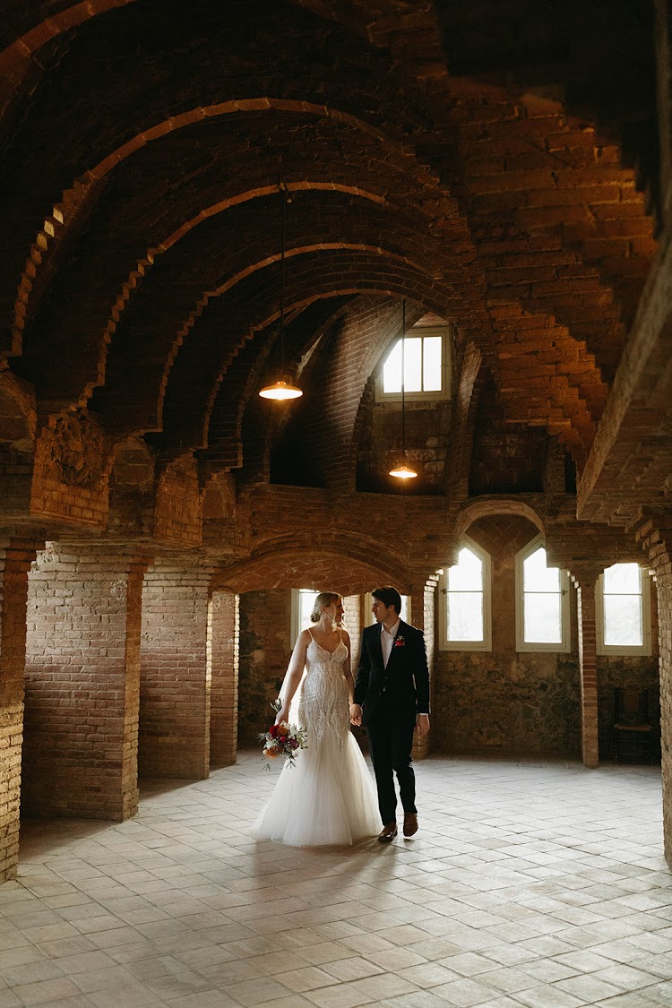 A bride and groom walking through the brick-vaulted attic of Bellesguard Tower, a Gaudí building in Barcelona