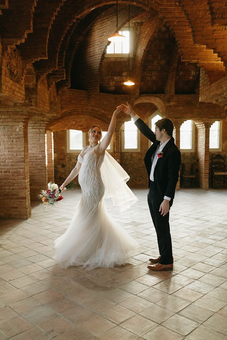 A couple dancing in the Gaudí brick attic of Bellesguard Tower in Barcelona, the bride's veil floating