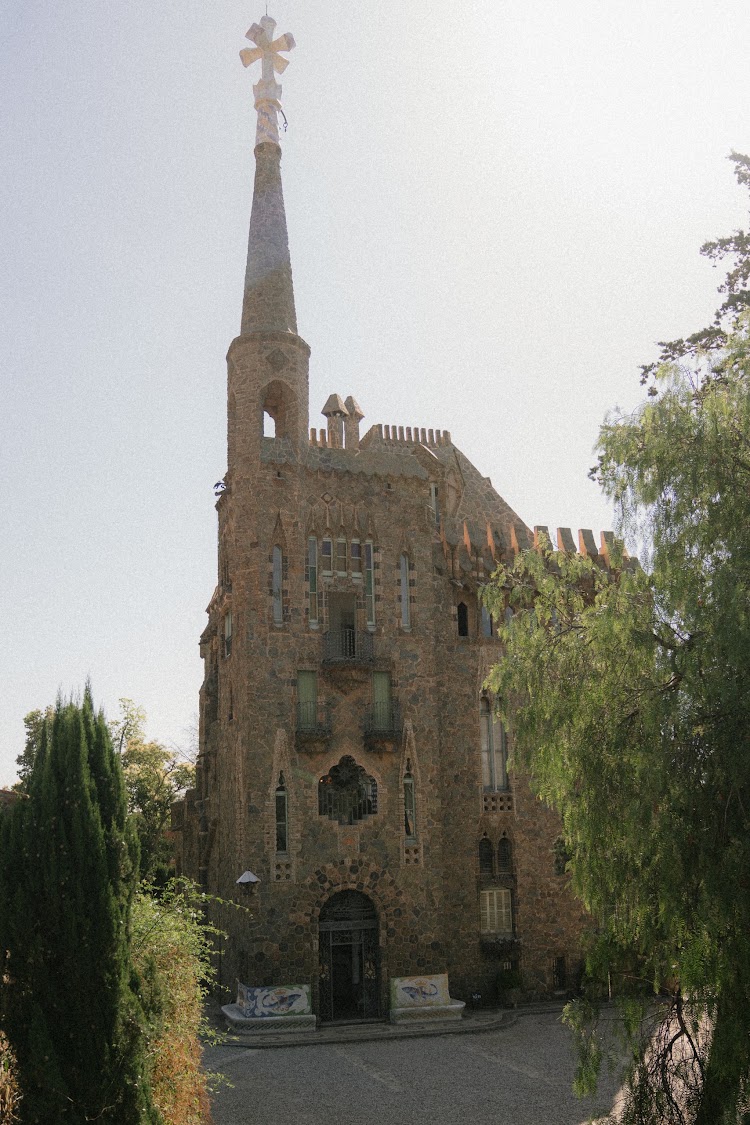 Bellesguard Tower in Barcelona, Gaudí's medieval-style stone tower with a cross-topped spire, seen from the garden