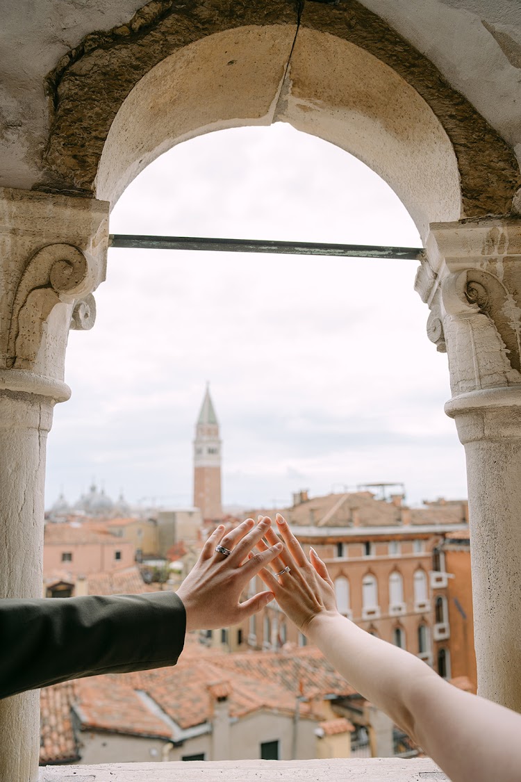 Hands joined under an arch, with a bell tower of Venice beyond
