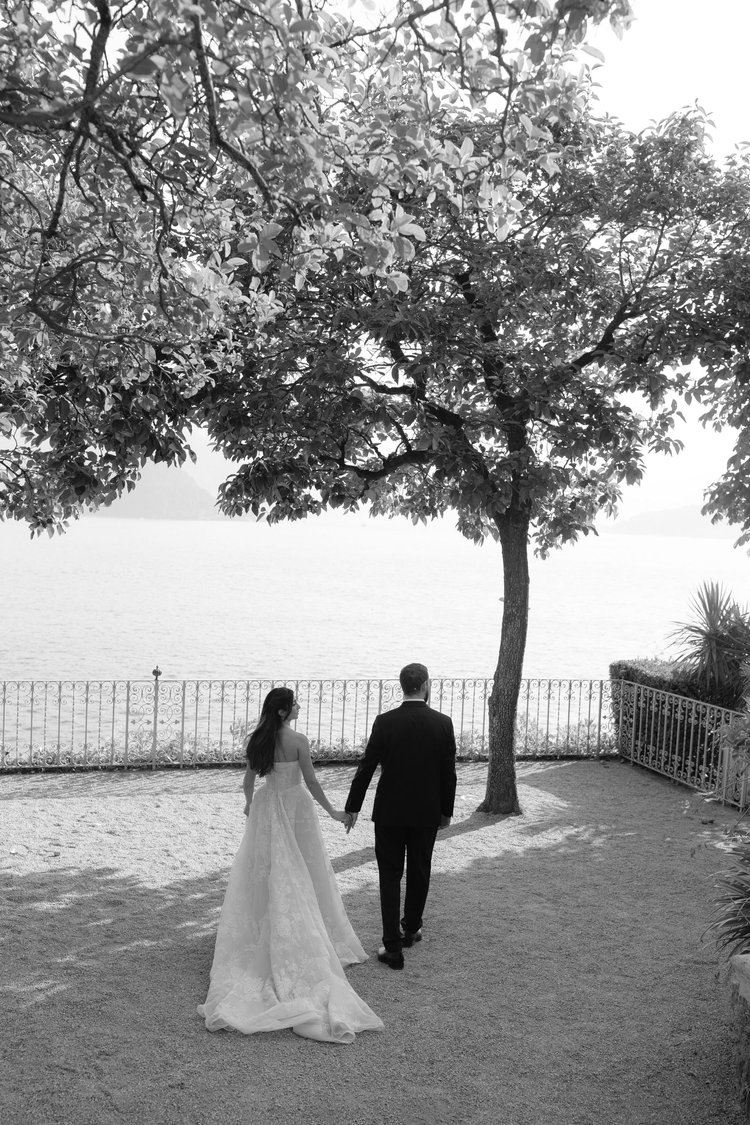 A couple walking towards the lake under the trees