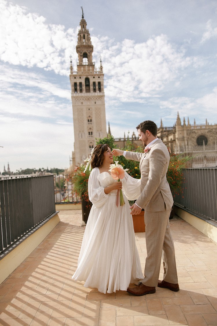 A bride and groom standing together on the terrace of EME Catedral Mercer in Seville, Spain, with the Giralda and Cathedral behind