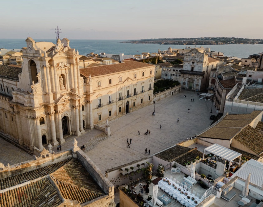 Aerial view of the Terraza Killiche rooftop terrace overlooking the baroque cathedral and piazza in Ortigia, Sicily, set up for an elopement aperitif at golden hour