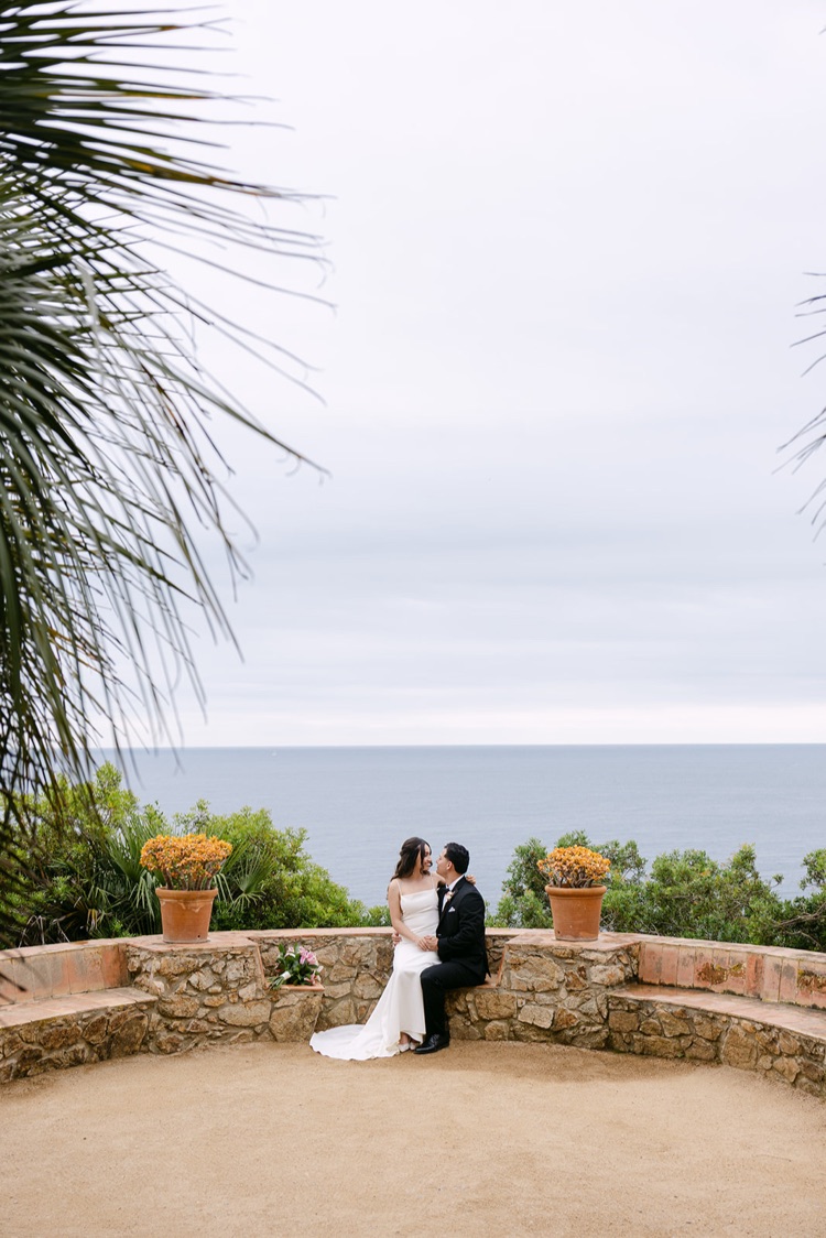 A couple sitting together on a stone wall above the sea in Marimurtra Botanic Gardens, Costa Brava