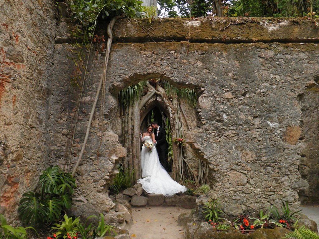 A couple standing in the root-covered stone archway of the Ruin Chapel at Monserrate Palace in Sintra, Portugal