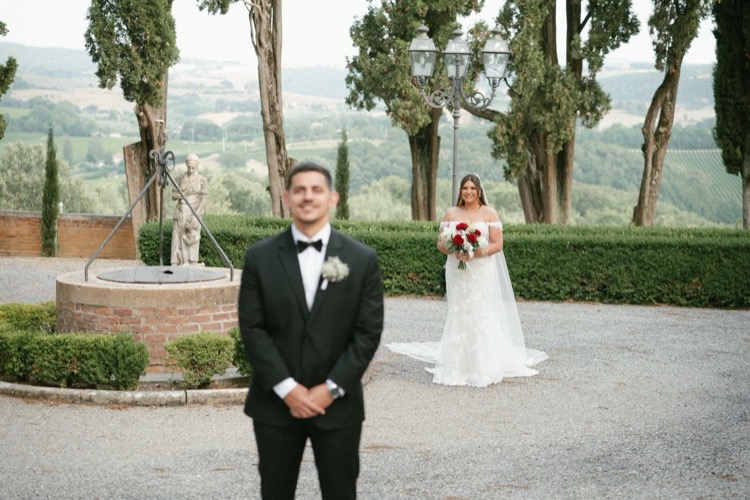 A groom waiting for his bride in the courtyard garden at Villa Poggiano, Tuscany, with cypress trees and countryside beyond