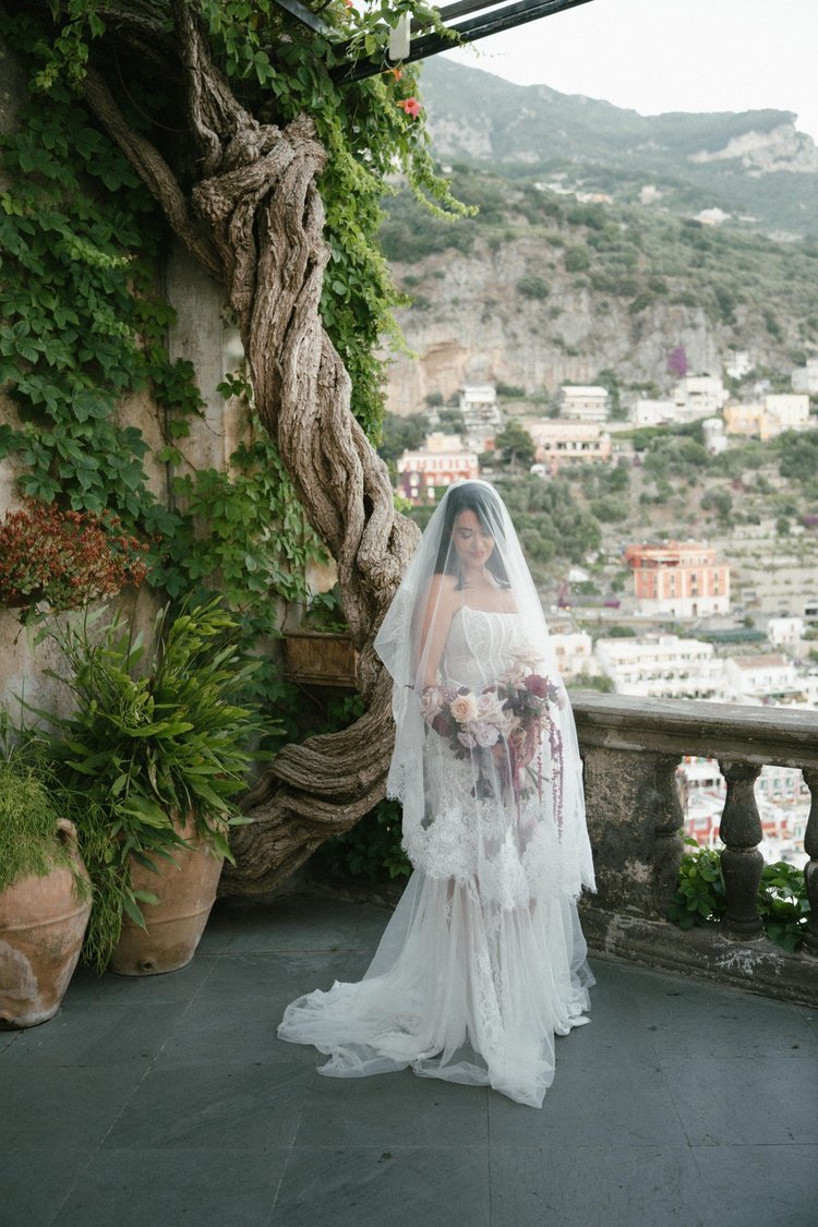 A bride beneath a vine-covered arch above Positano